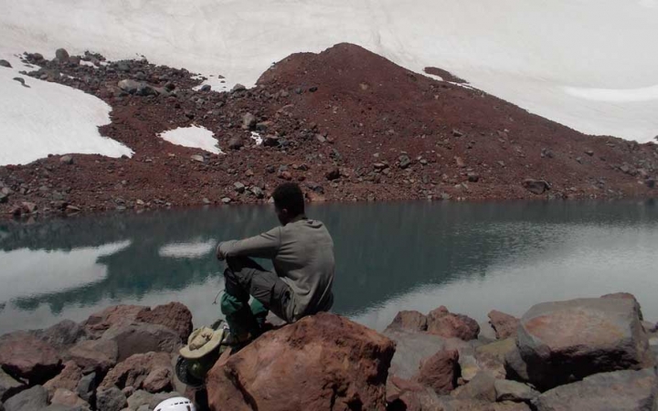 a student sits on a rock beside an alpine lake, reflecting on their outward bound experience.